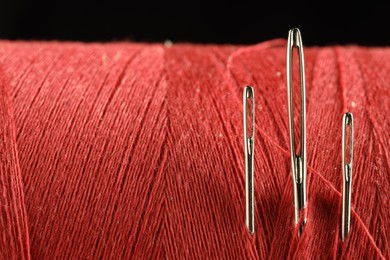 Spool of red sewing thread with needles on black background, macro view