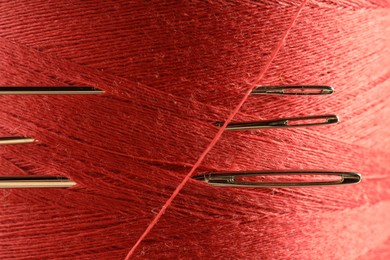 Spool of red sewing thread with needles, macro view