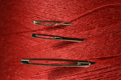 Photo of Spool of red sewing thread with needles, macro view