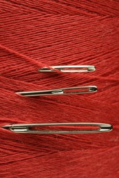 Photo of Spool of red sewing thread with needles, macro view