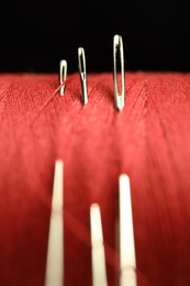 Spool of red sewing thread with needles on black background, macro view