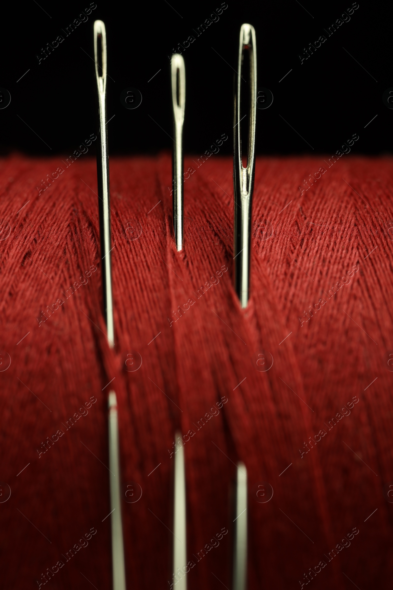 Photo of Spool of red sewing thread with needles on black background, macro view