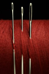 Photo of Spool of red sewing thread with needles on black background, macro view