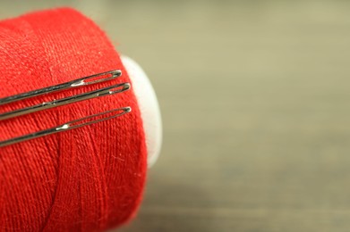 Photo of Spool of red sewing thread with needles on blurred background, closeup. Space for text