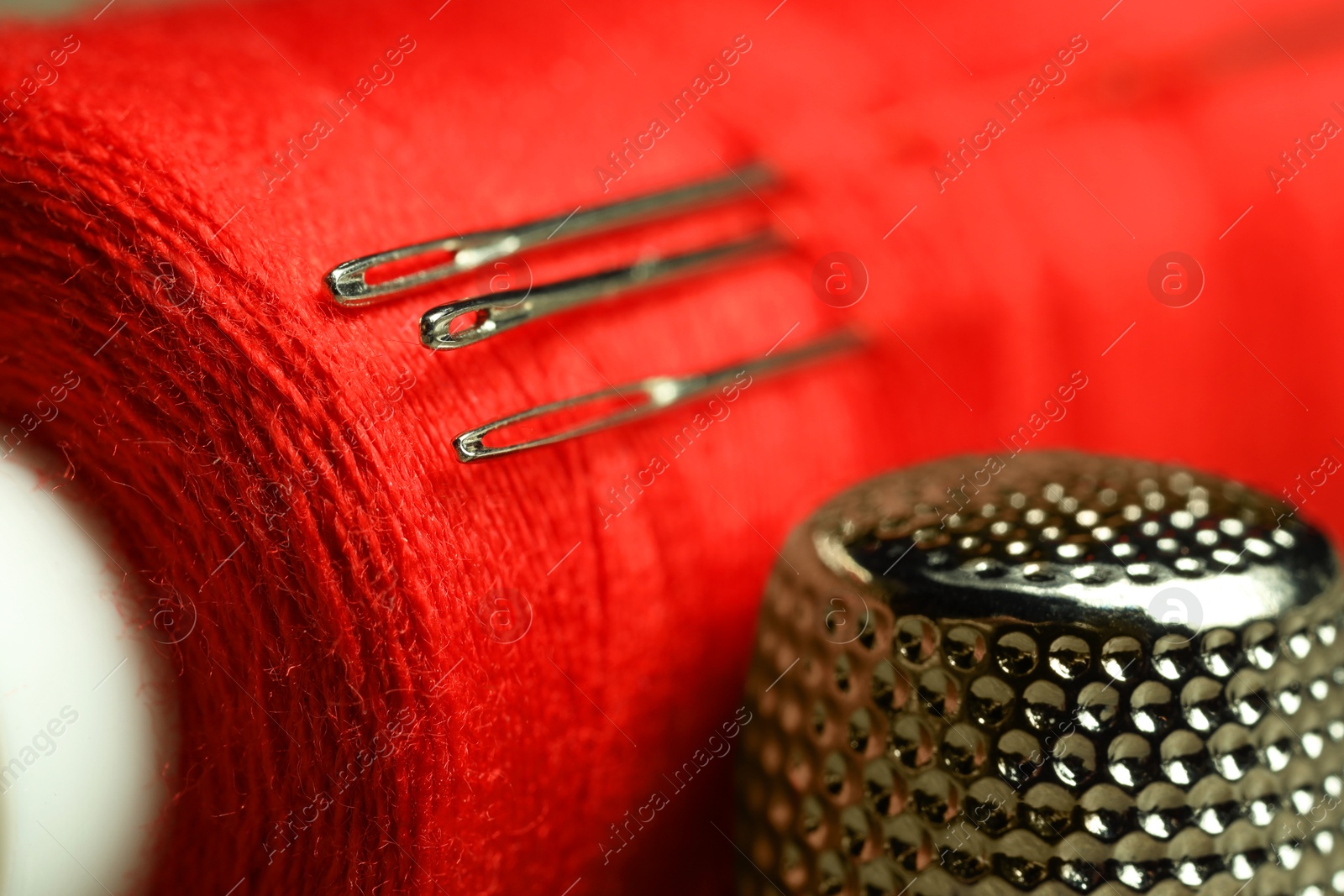 Photo of Spool of red sewing thread with needles and thimble, closeup