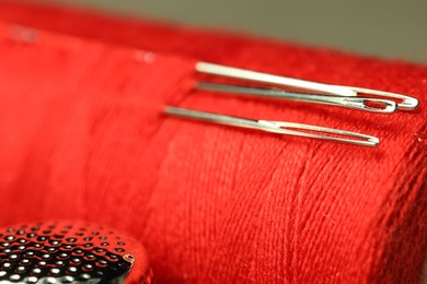 Photo of Spool of red sewing thread with needles and thimble, closeup