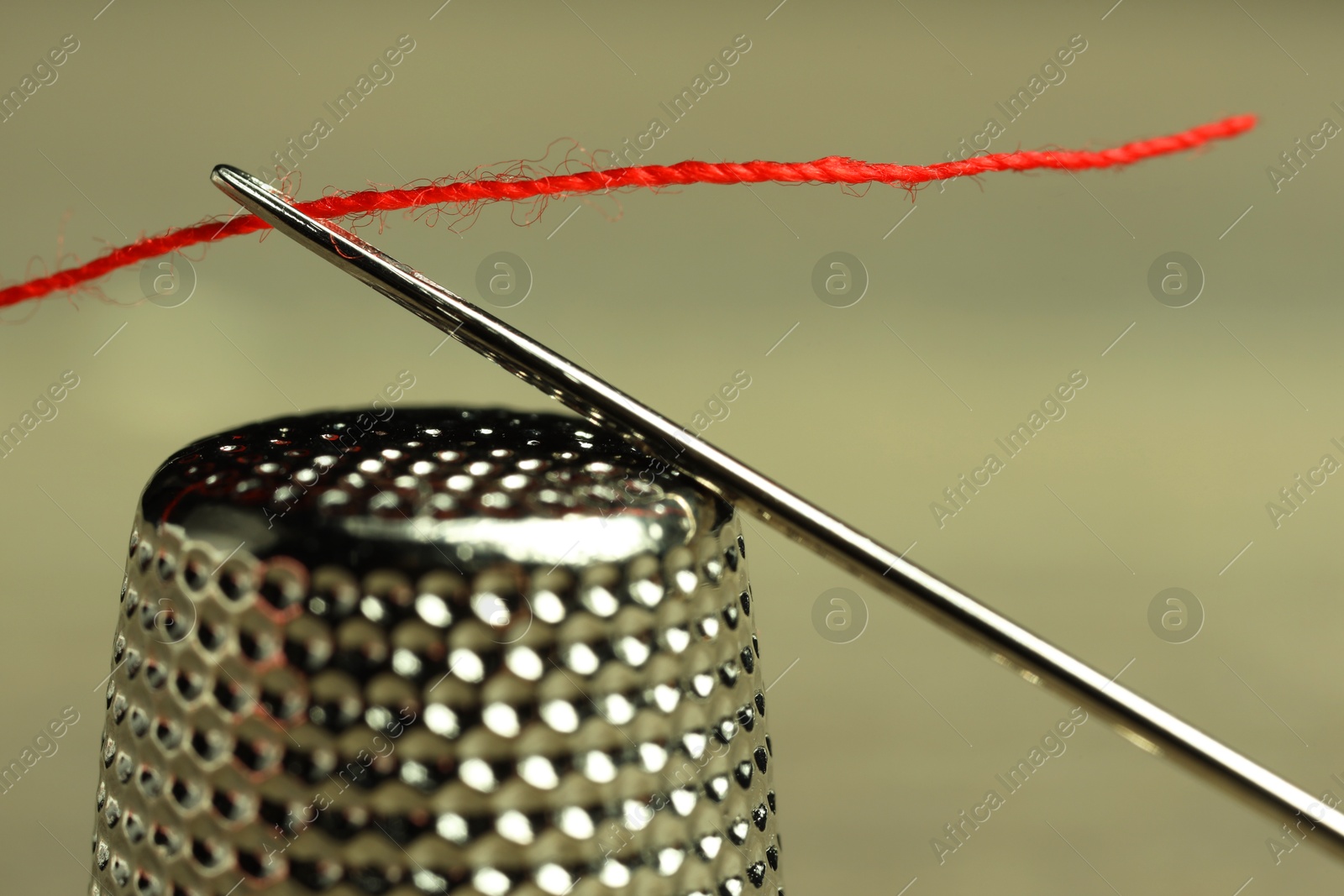 Photo of Sewing needle with red thread and thimble on blurred background, closeup