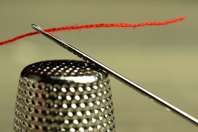 Photo of Sewing needle with red thread and thimble on blurred background, closeup