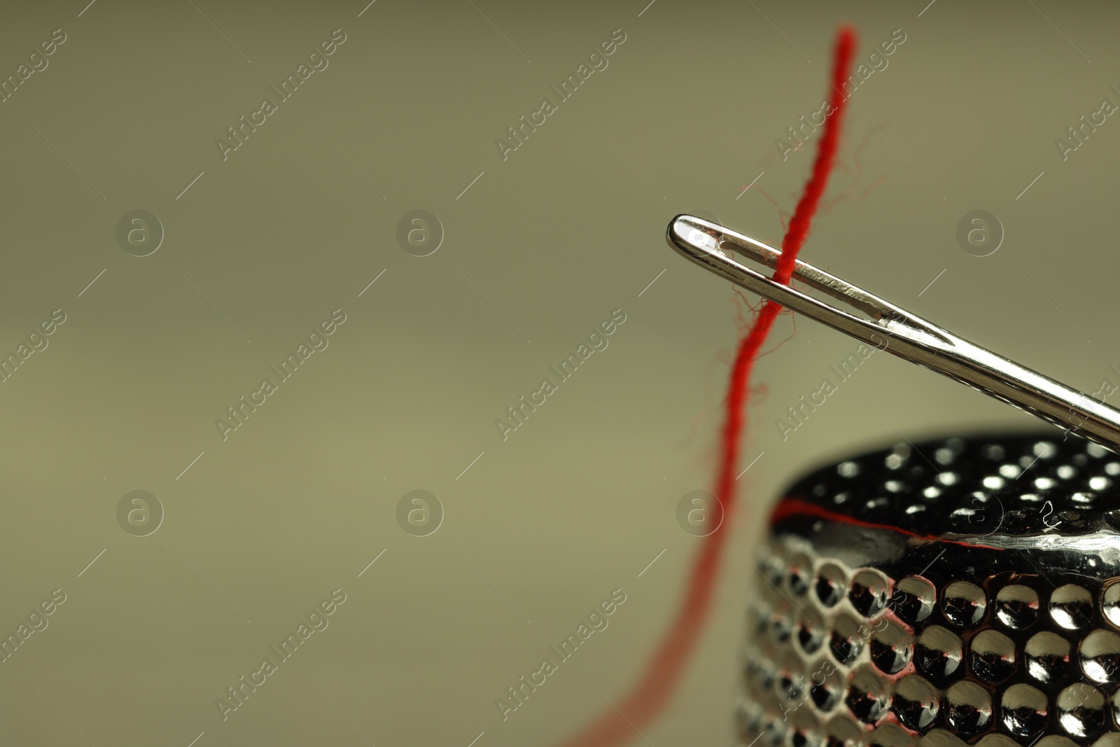 Photo of Sewing needle with red thread and thimble on blurred background, closeup. Space for text