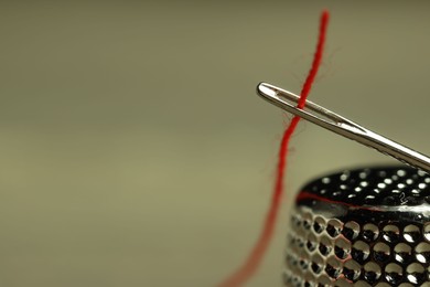 Photo of Sewing needle with red thread and thimble on blurred background, closeup. Space for text