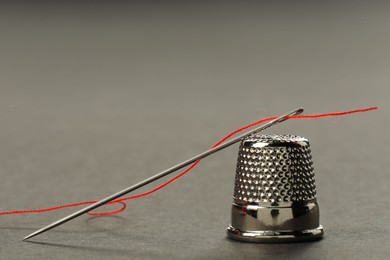 Sewing needle with red thread and thimble on grey background, closeup. Space for text