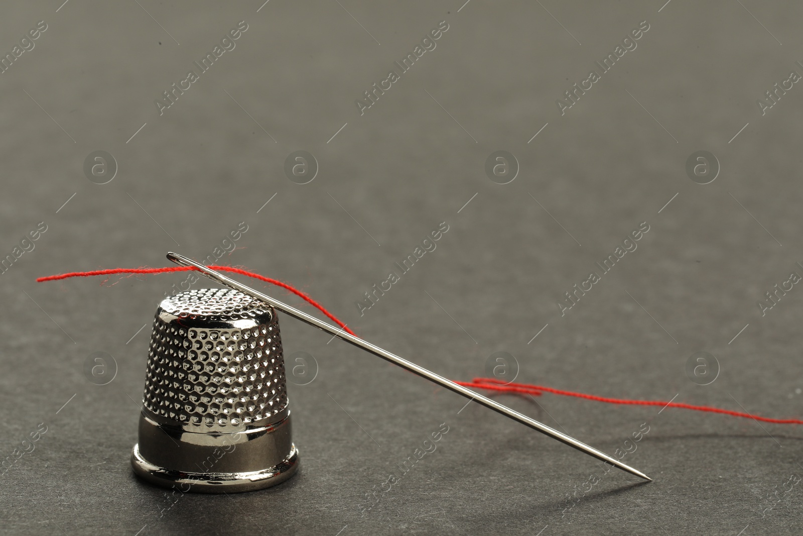 Photo of Sewing needle with red thread and thimble on grey background, closeup. Space for text