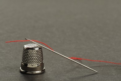 Sewing needle with red thread and thimble on grey background, closeup. Space for text