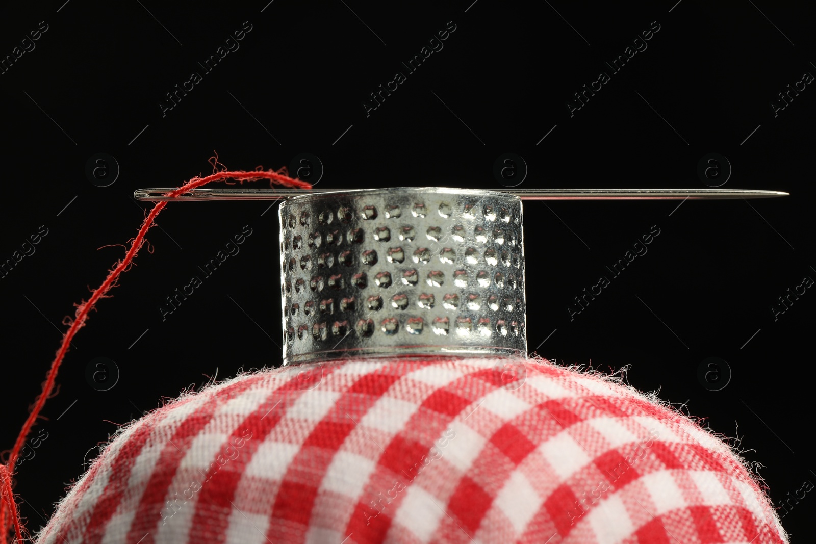 Photo of Sewing needle with red thread, thimble ring and pincushion on black background, closeup