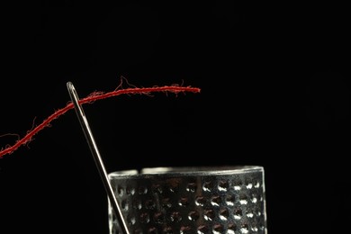 Photo of Sewing needle with red thread and thimble ring on black background, closeup