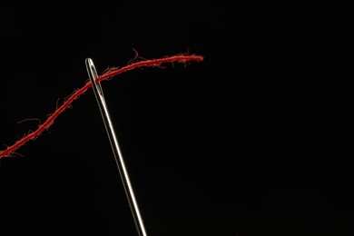 Photo of Sewing needle with red thread on black background, closeup. Space for text