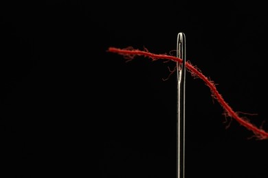 Photo of Sewing needle with red thread on black background, closeup. Space for text