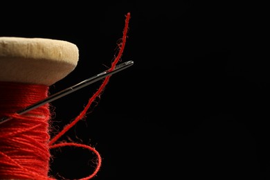 Photo of Spool of red sewing thread with needle on black background, closeup. Space for text