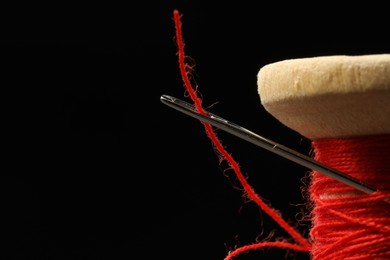 Photo of Spool of red sewing thread with needle on black background, closeup. Space for text