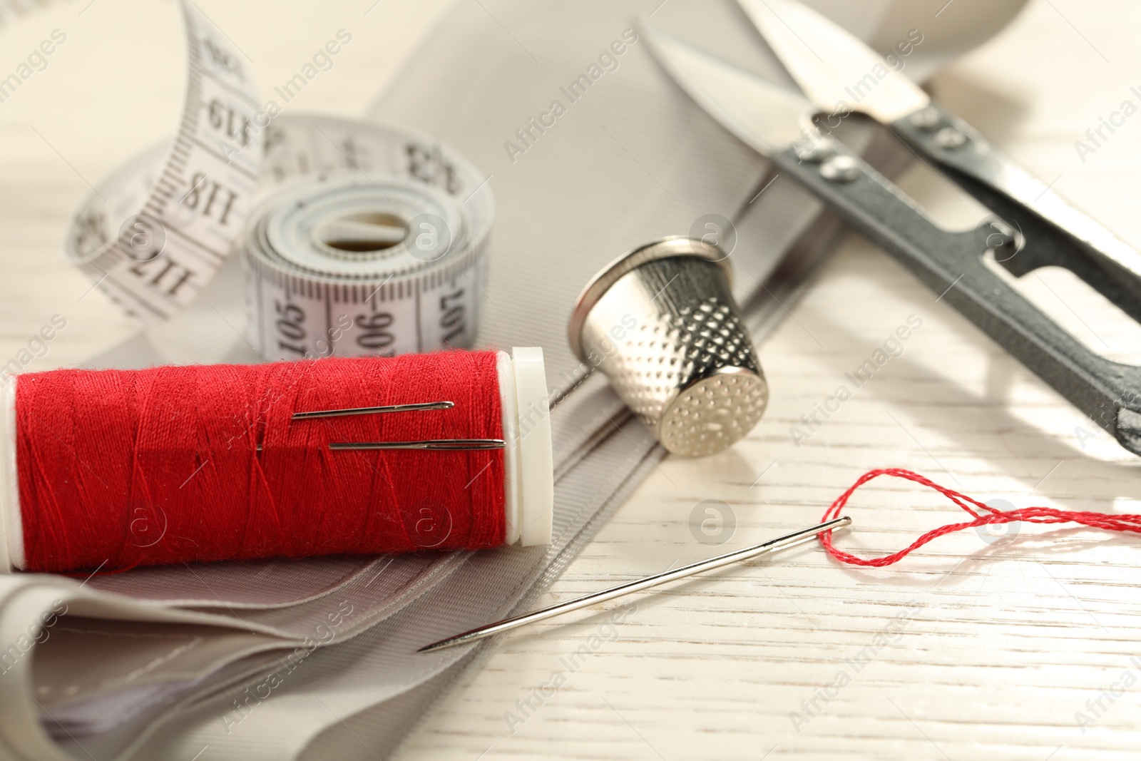 Photo of Different sewing tools on white wooden table, closeup