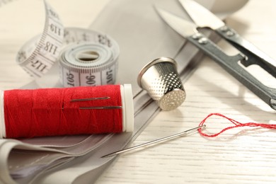 Photo of Different sewing tools on white wooden table, closeup