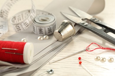 Different sewing tools on white wooden table, closeup