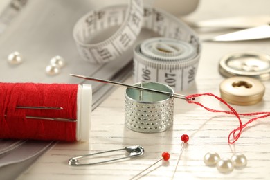 Photo of Different sewing tools on white wooden table, closeup