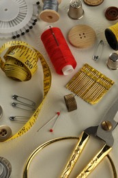 Different sewing tools on white textured table, above view