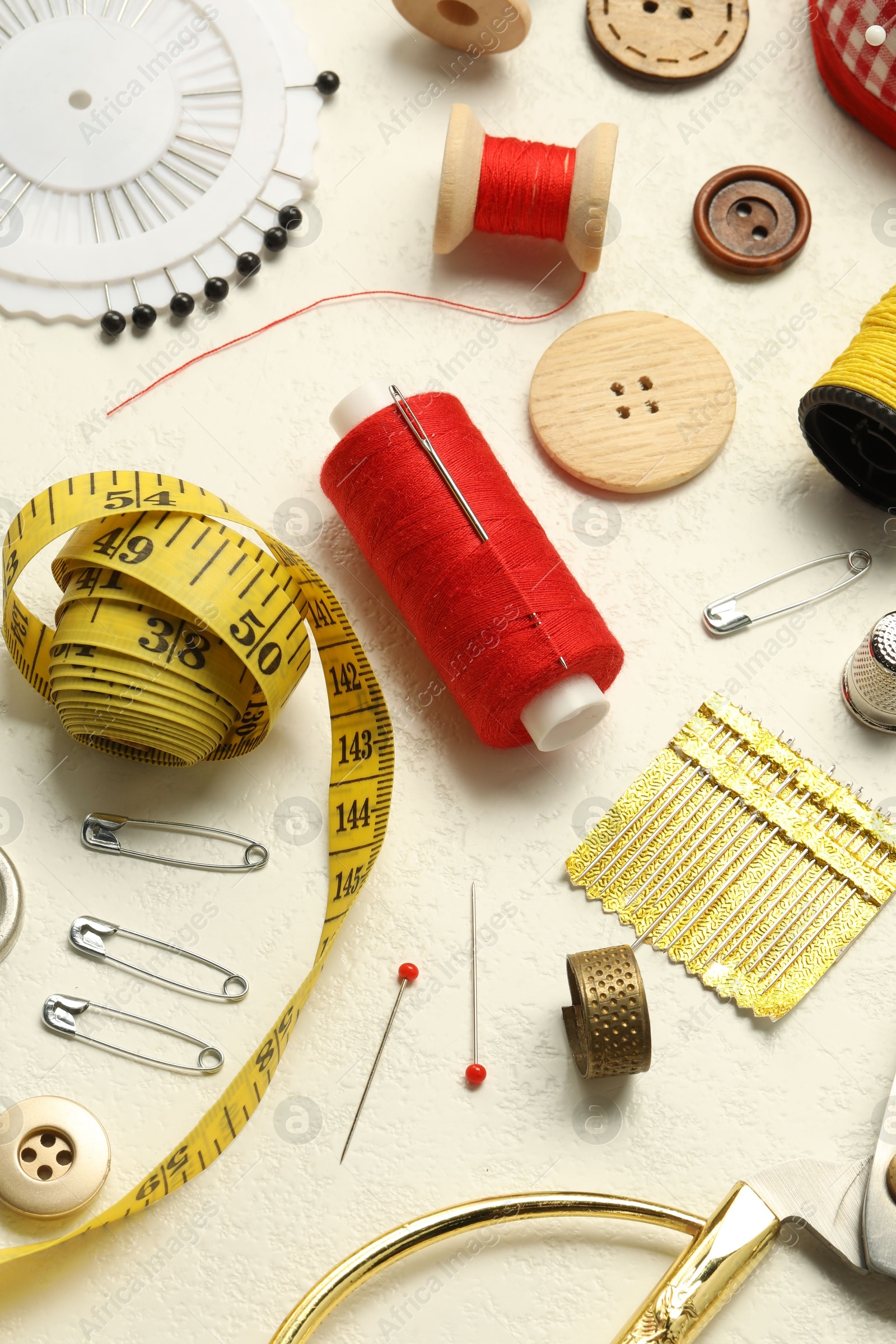 Photo of Different sewing tools on white textured table, above view