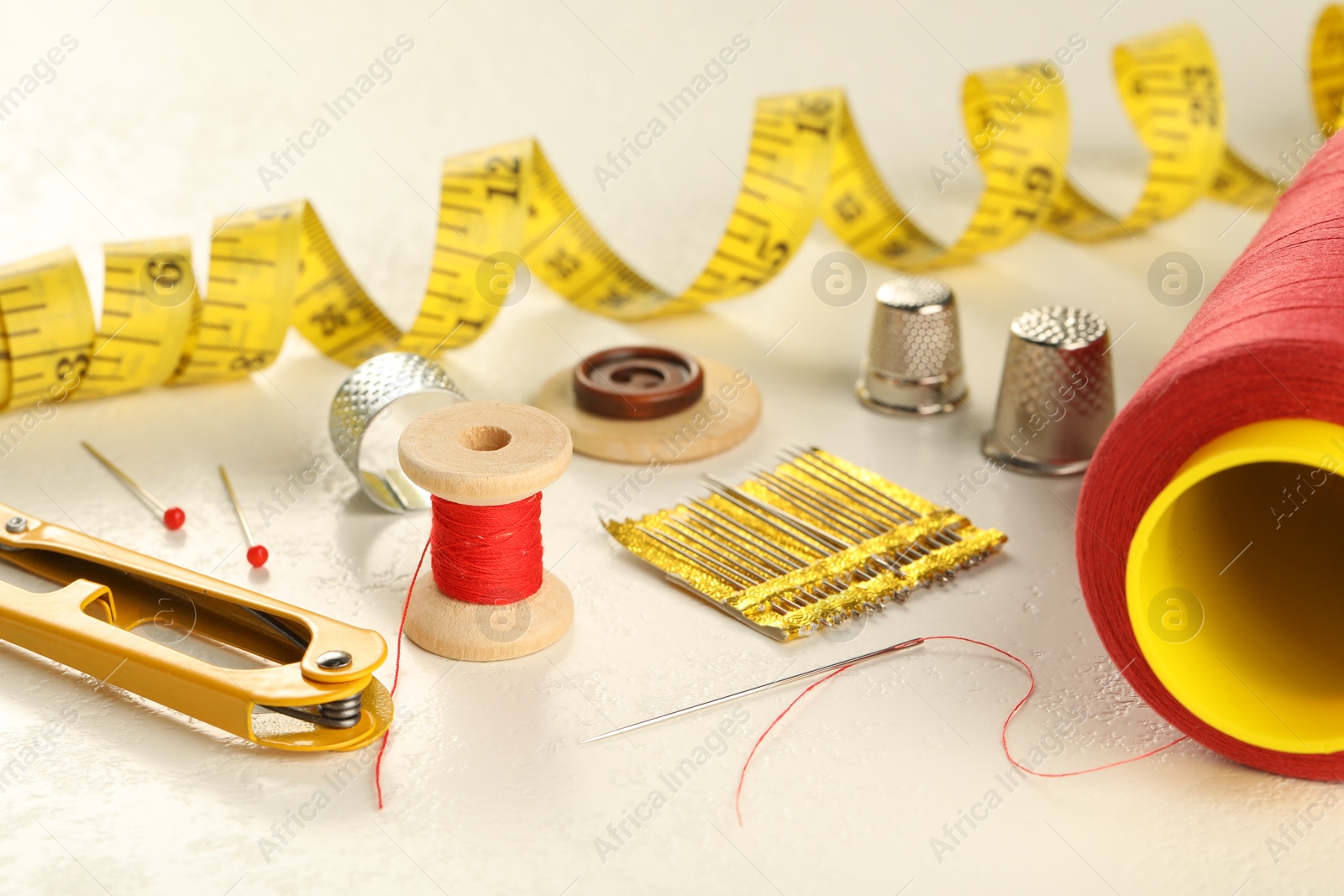 Photo of Different sewing tools on white textured table, closeup