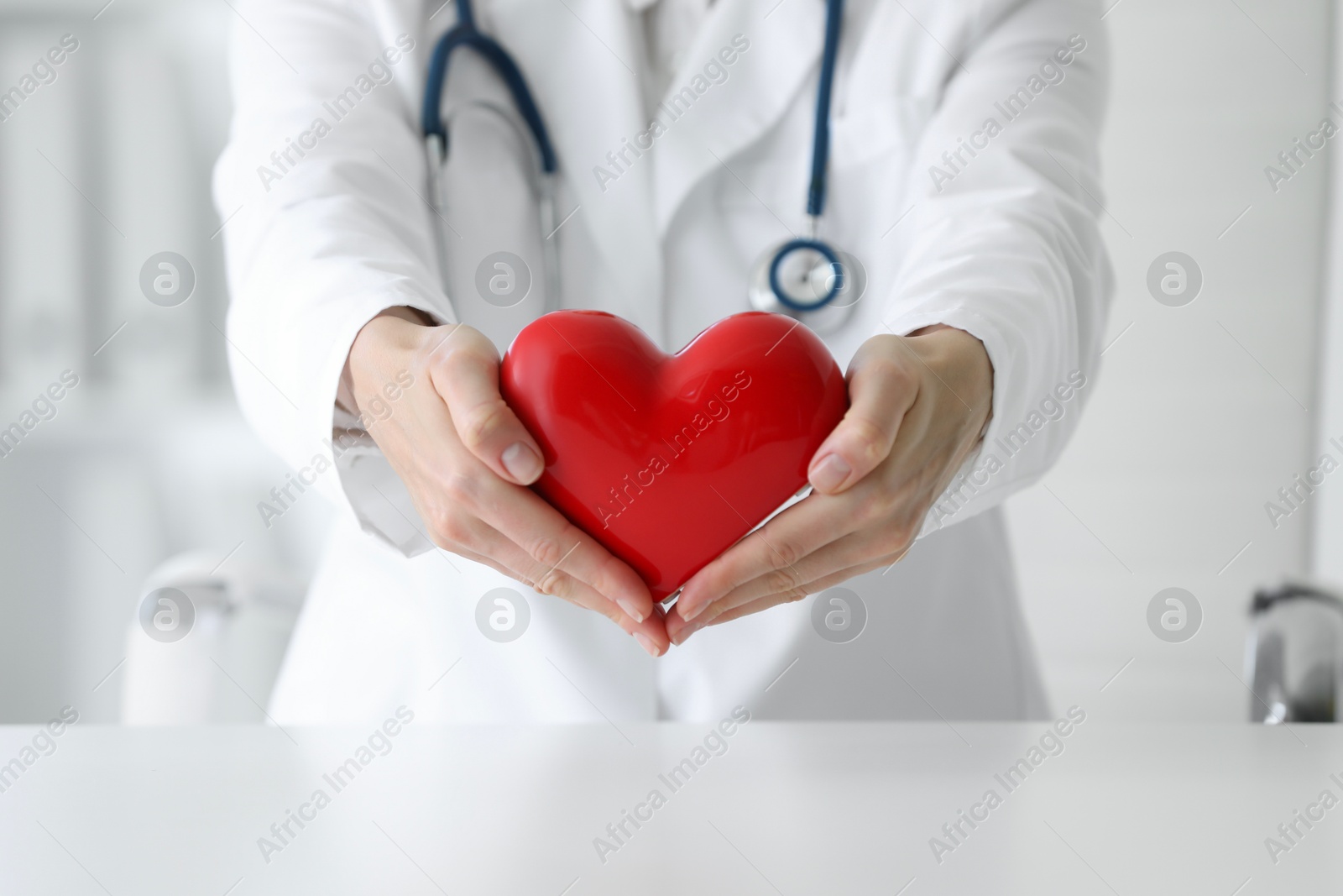 Photo of Doctor with red heart at table in clinic, closeup