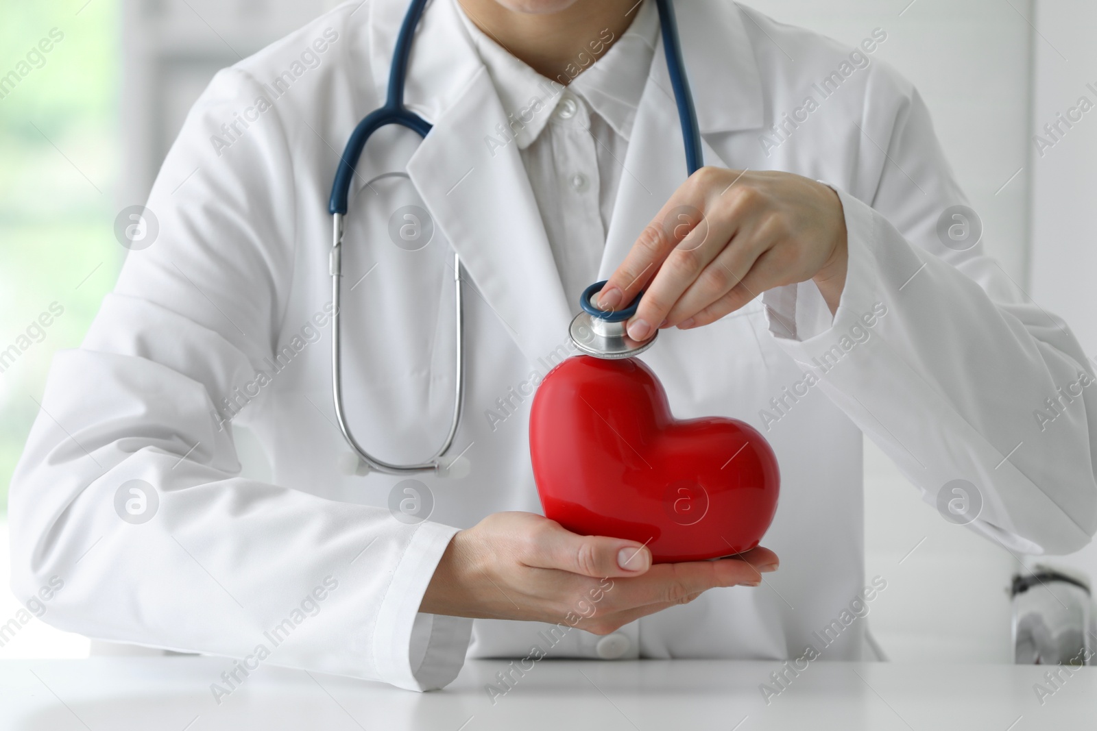 Photo of Doctor with stethoscope and red heart at table in clinic, closeup