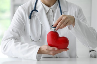 Doctor with stethoscope and red heart at table in clinic, closeup