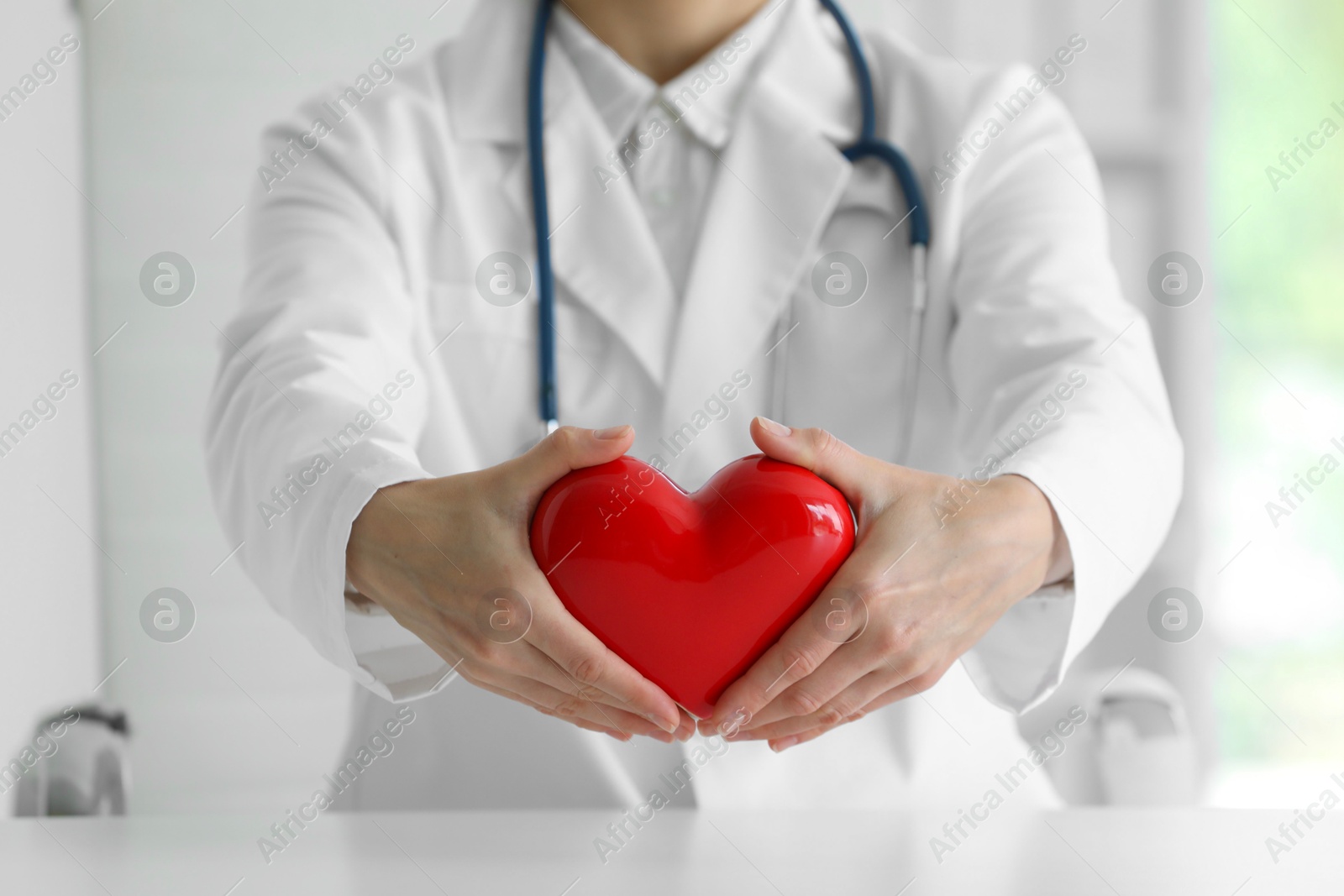 Photo of Doctor with red heart at table in clinic, closeup