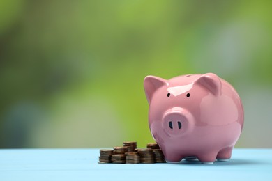 Photo of Pink piggy bank and stacks of coins on light blue table against blurred background, space for text