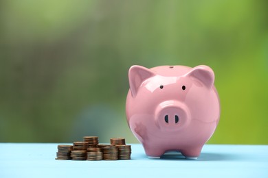 Photo of Pink piggy bank and stacks of coins on light blue table against blurred background