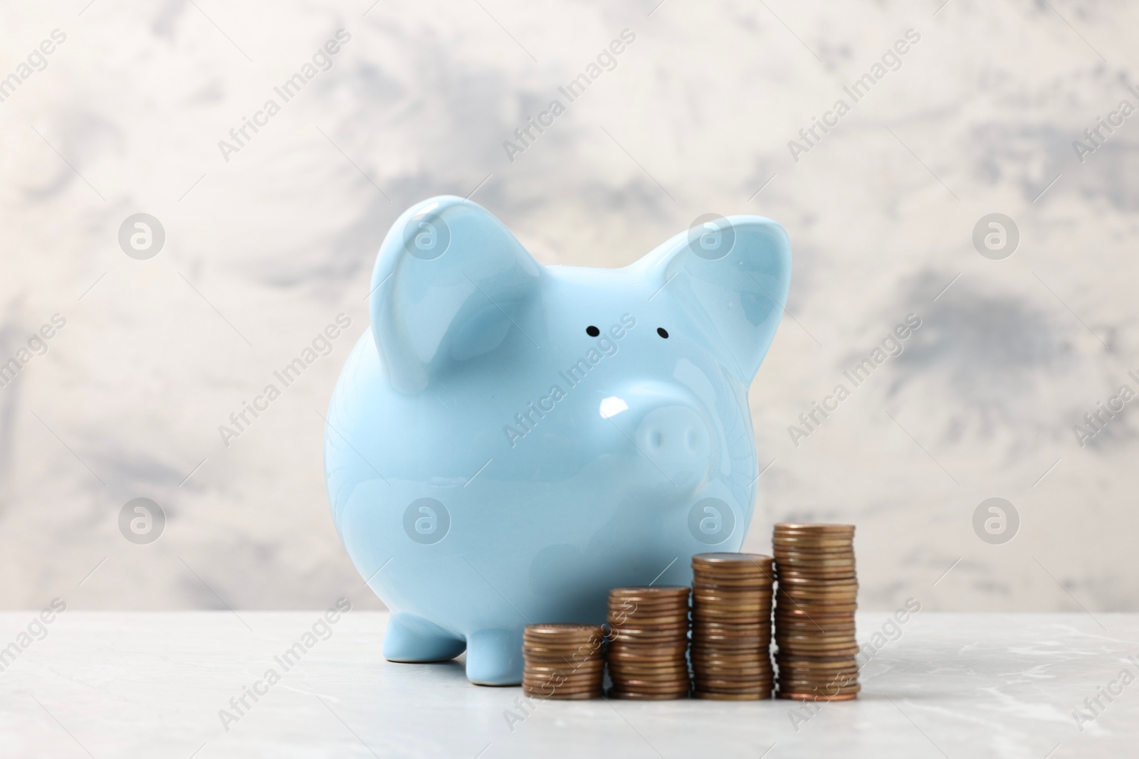 Photo of Blue piggy bank and stacks of coins on light marble table