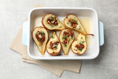 Photo of Tasty baked pears with nuts, blue cheese, thyme and honey in baking dish on light grey table, top view