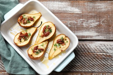 Tasty baked pears with nuts, blue cheese, thyme and honey in baking dish on wooden table, top view. Space for text