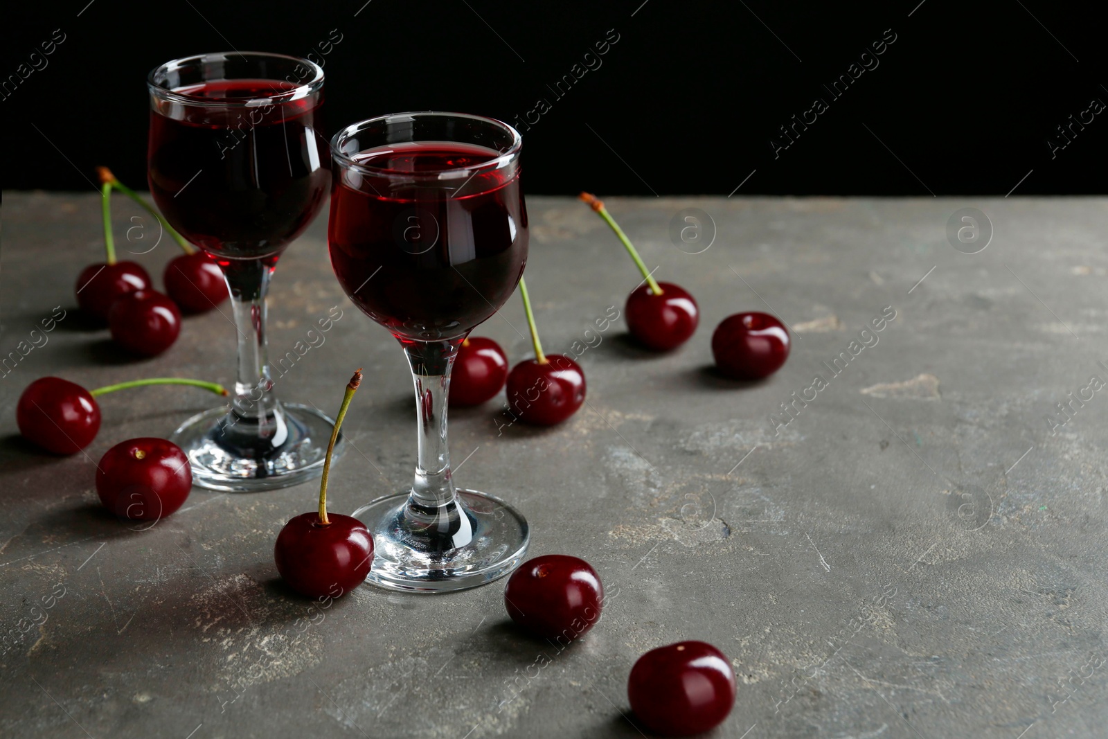 Photo of Delicious cherry liqueur in glasses and fresh berries on grey background, space for text