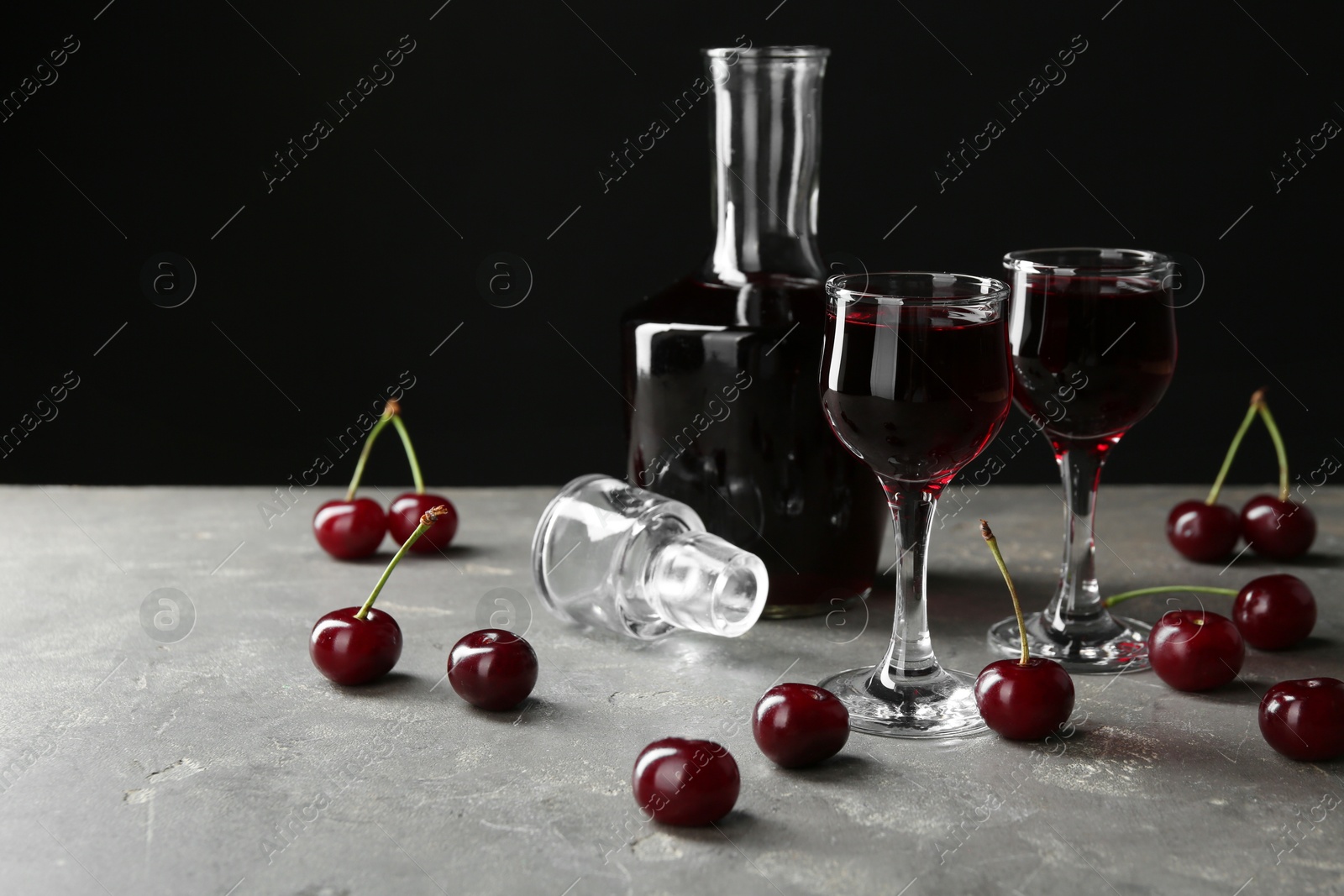 Photo of Delicious cherry liqueur in glasses, decanter and fresh berries on grey table