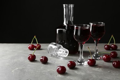 Delicious cherry liqueur in glasses, decanter and fresh berries on grey table