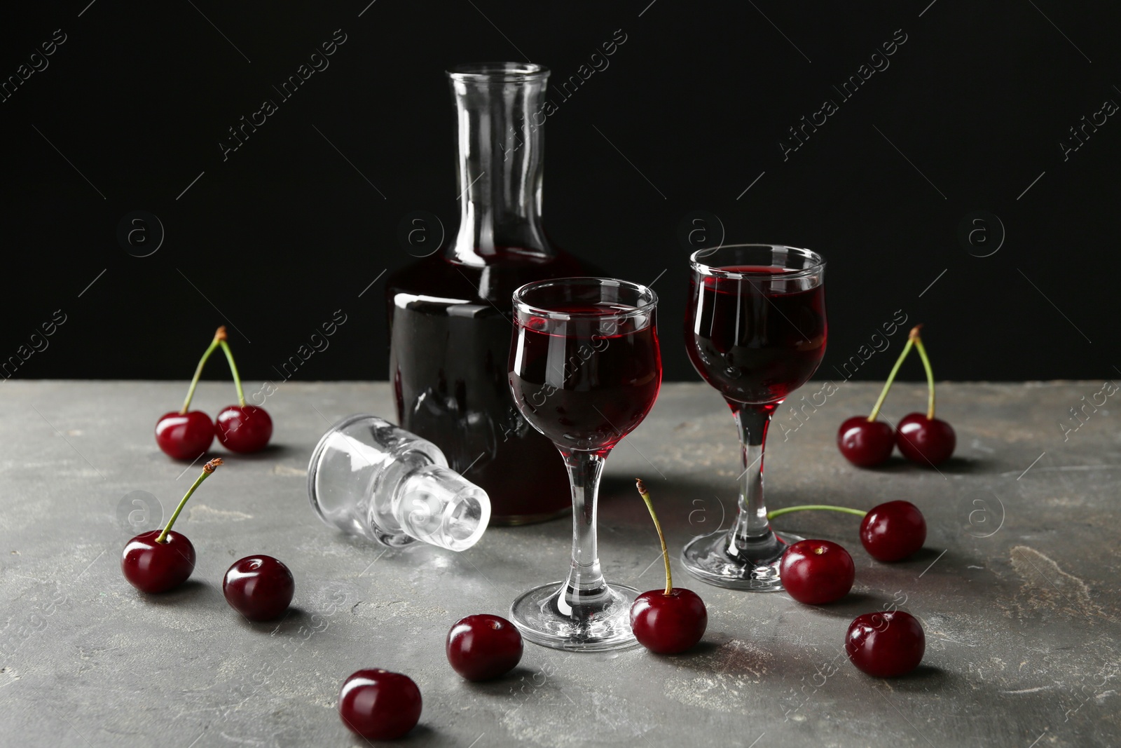 Photo of Delicious cherry liqueur in glasses, decanter and fresh berries on grey table