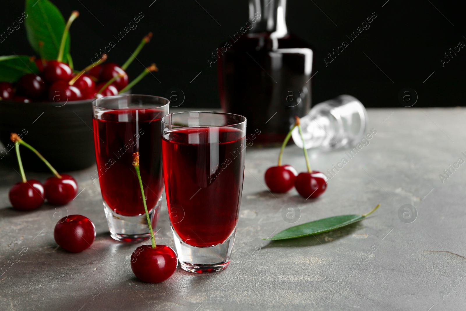 Photo of Delicious cherry liqueur in shot glasses and fresh berries on grey table