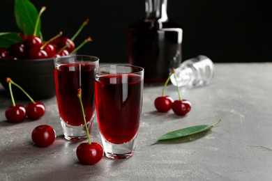 Photo of Delicious cherry liqueur in shot glasses and fresh berries on grey table