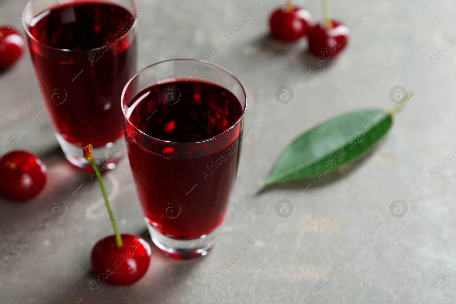 Photo of Delicious cherry liqueur in shot glasses and fresh berries on grey table, closeup