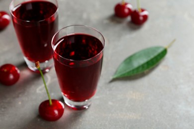 Photo of Delicious cherry liqueur in shot glasses and fresh berries on grey table, closeup