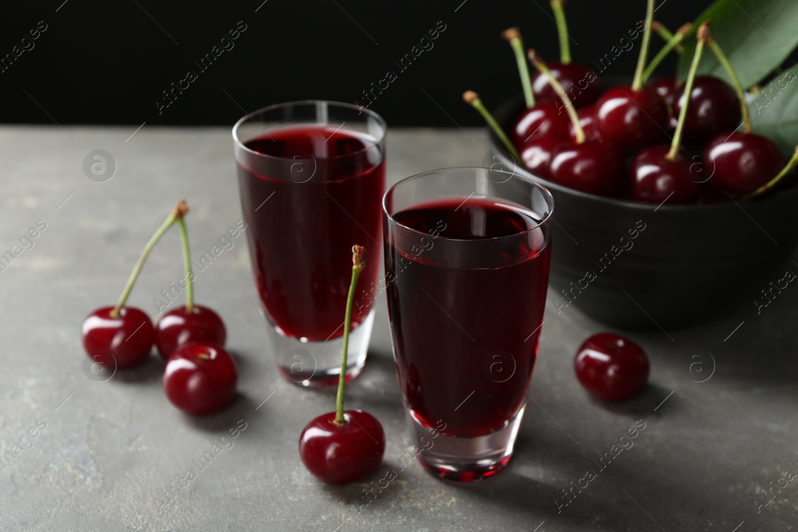 Photo of Delicious cherry liqueur in shot glasses and fresh berries on grey table