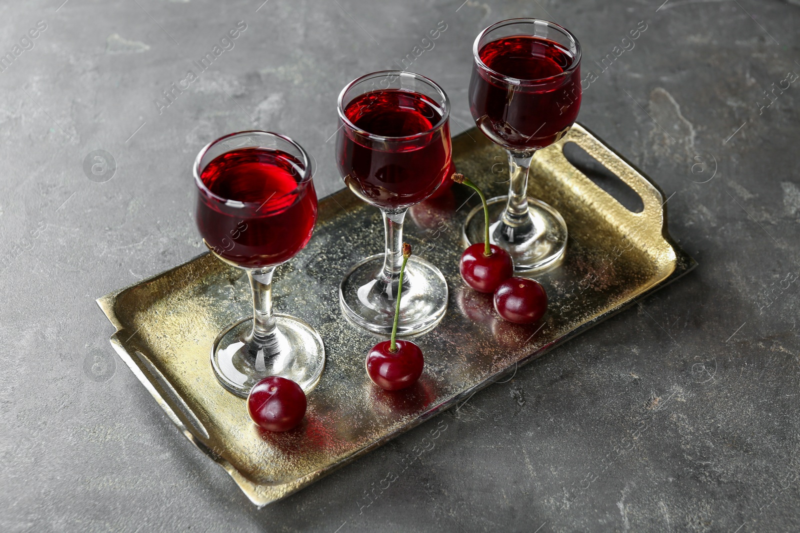 Photo of Delicious cherry liqueur in glasses and fresh berries on grey table