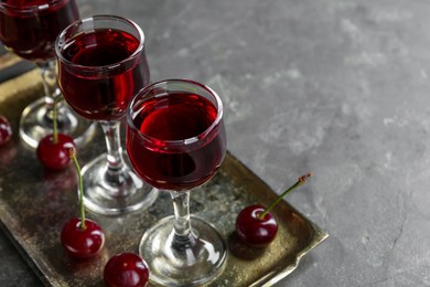 Photo of Delicious cherry liqueur in glasses and fresh berries on grey table, space for text